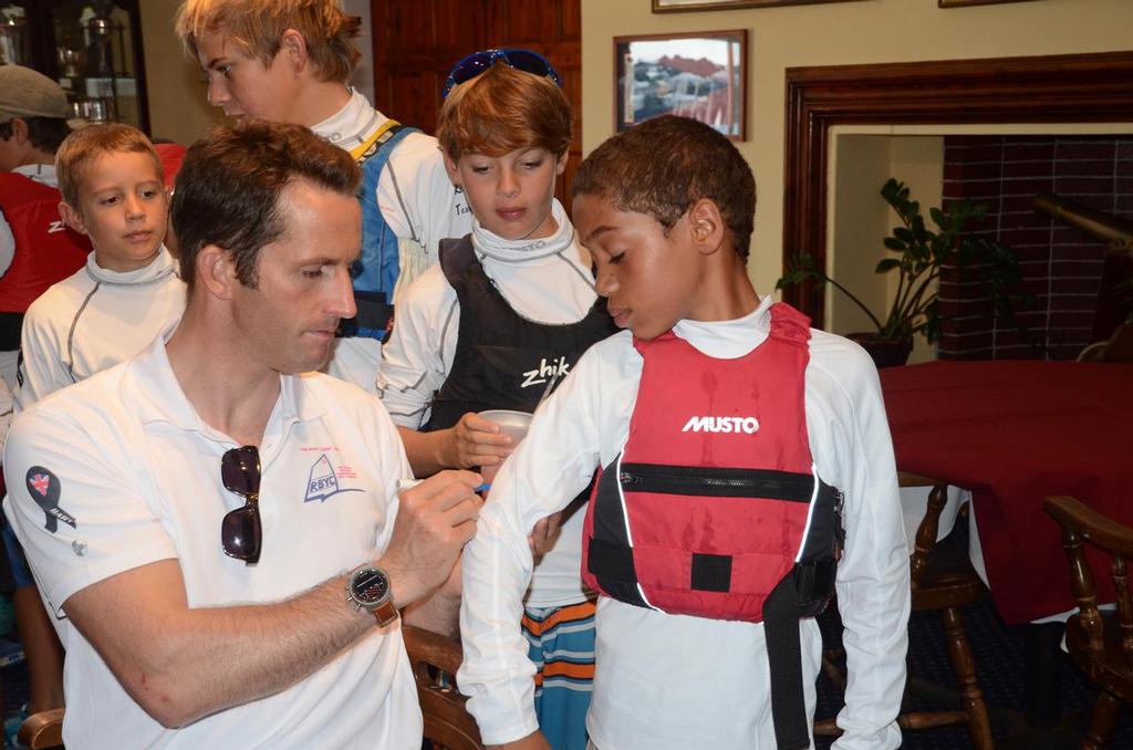 Ainslie autographs Bermudian Jay Hall’s BART Clinic shirt.The Ben Ainslie Racing Team (BART) sailing clinic for young Royal Bermuda YC and Bermuda Optimist Dinghy Association (BODA) Squad sailors raised around $3000 for the Andrew ’Bart’ Simpson Sailing Foundation (ASSF). The price of admission to the clinic was that each young sailor purchased a ASSF rashguard shirt. © Talbot Wilson
